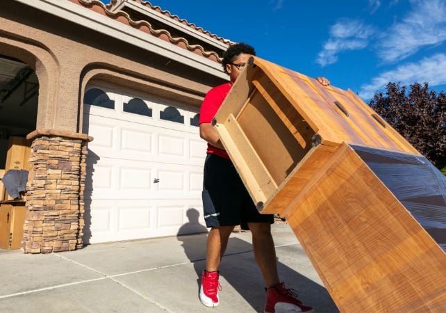 Person moves large wooden furniture outside garage