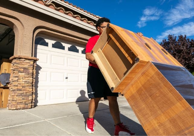 Person moving a wooden dresser outdoors.