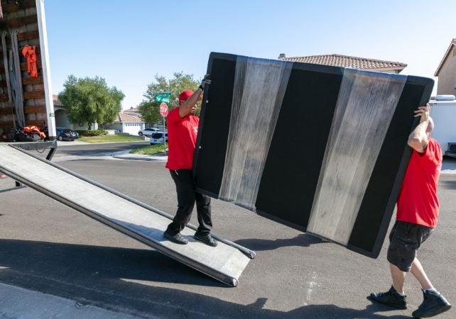 Movers lifting wrapped couch into truck on ramp.