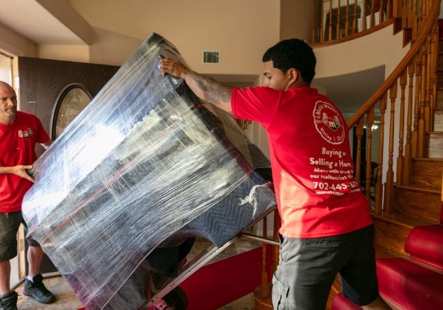 Movers transporting wrapped furniture indoors.